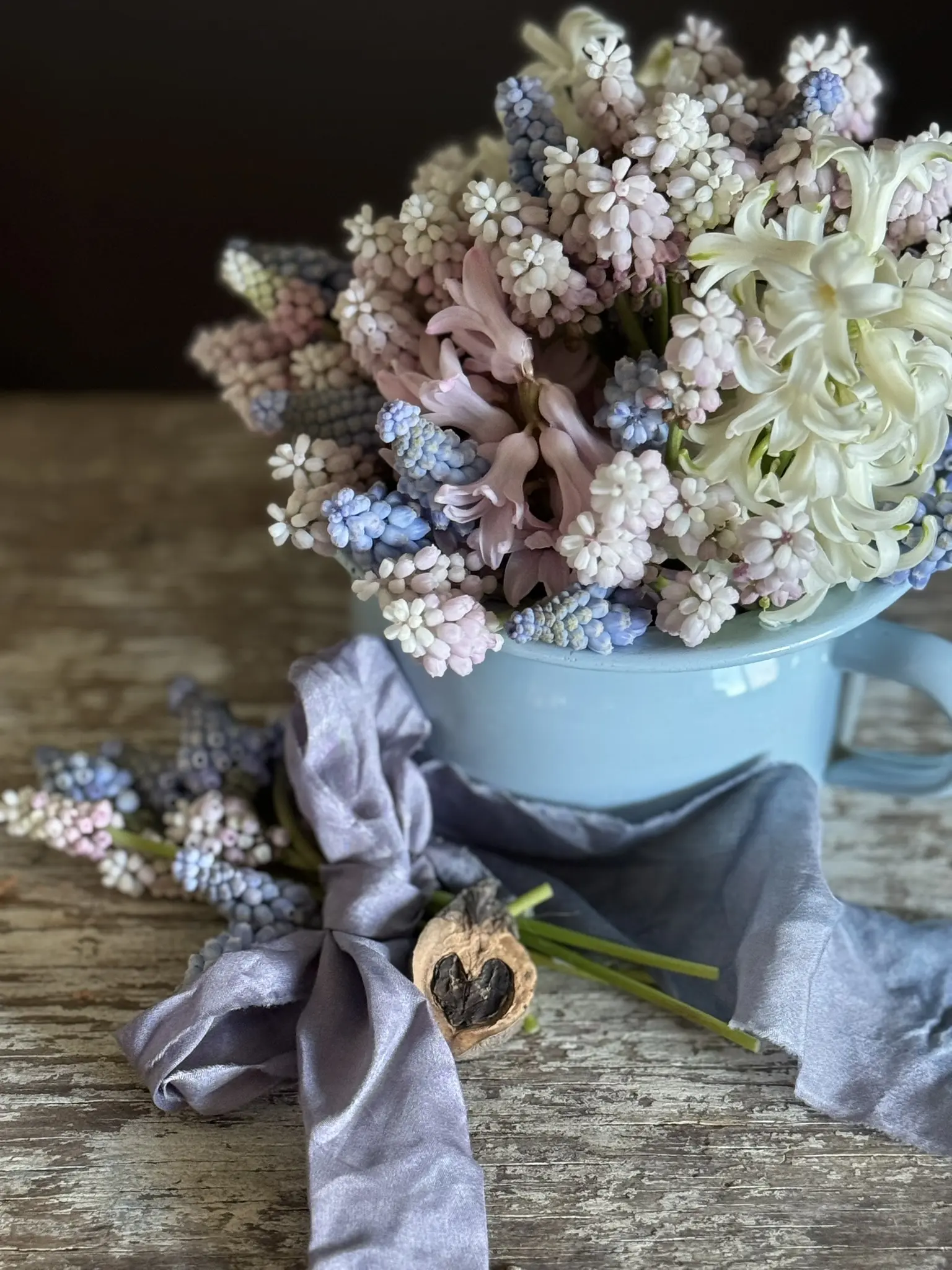 A bouquet of dried flowers wrapped in fabric beside a blue pot of dried flowers.