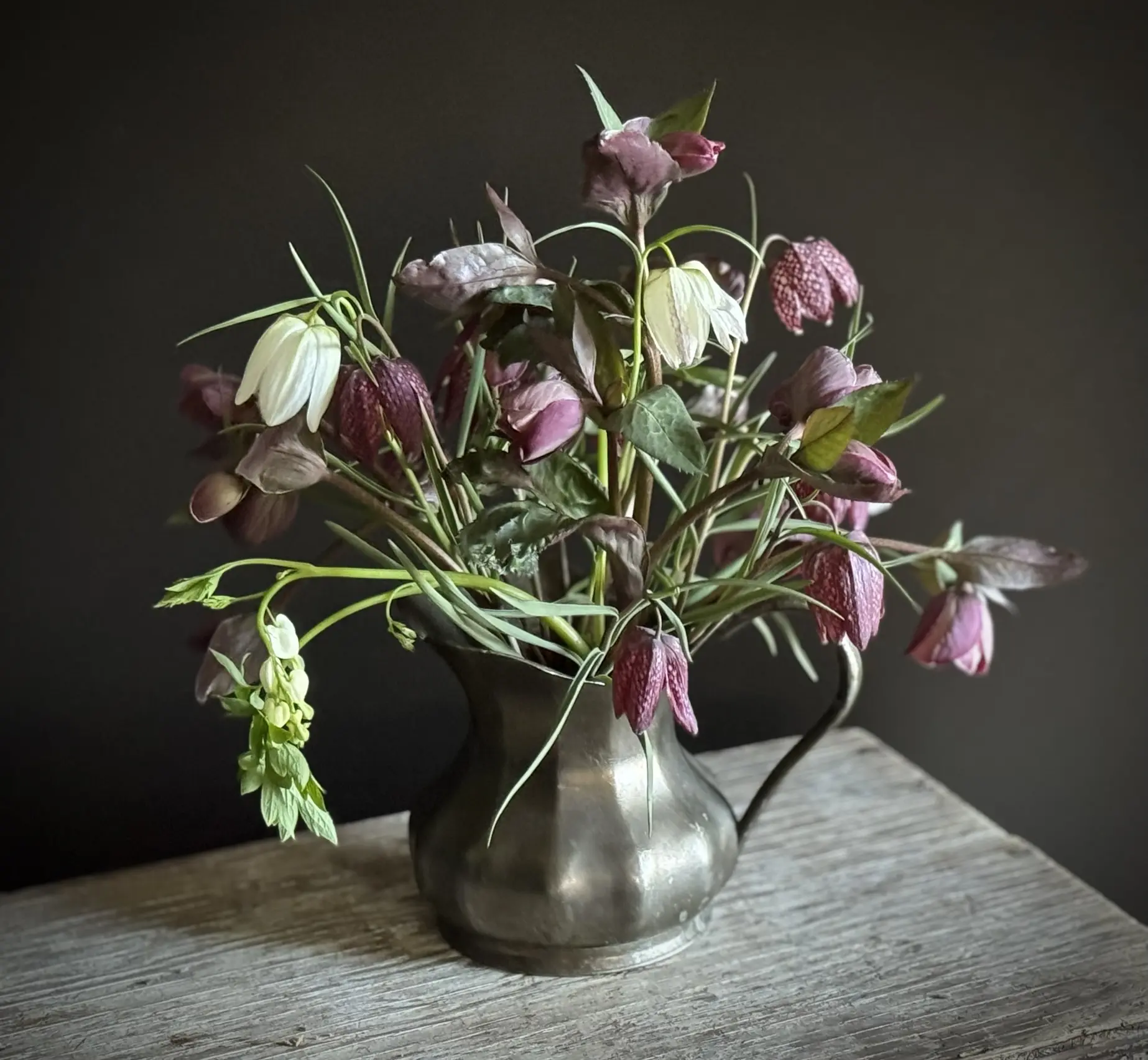 A bouquet of wilted purple and green flowers in a tarnished metal vase.