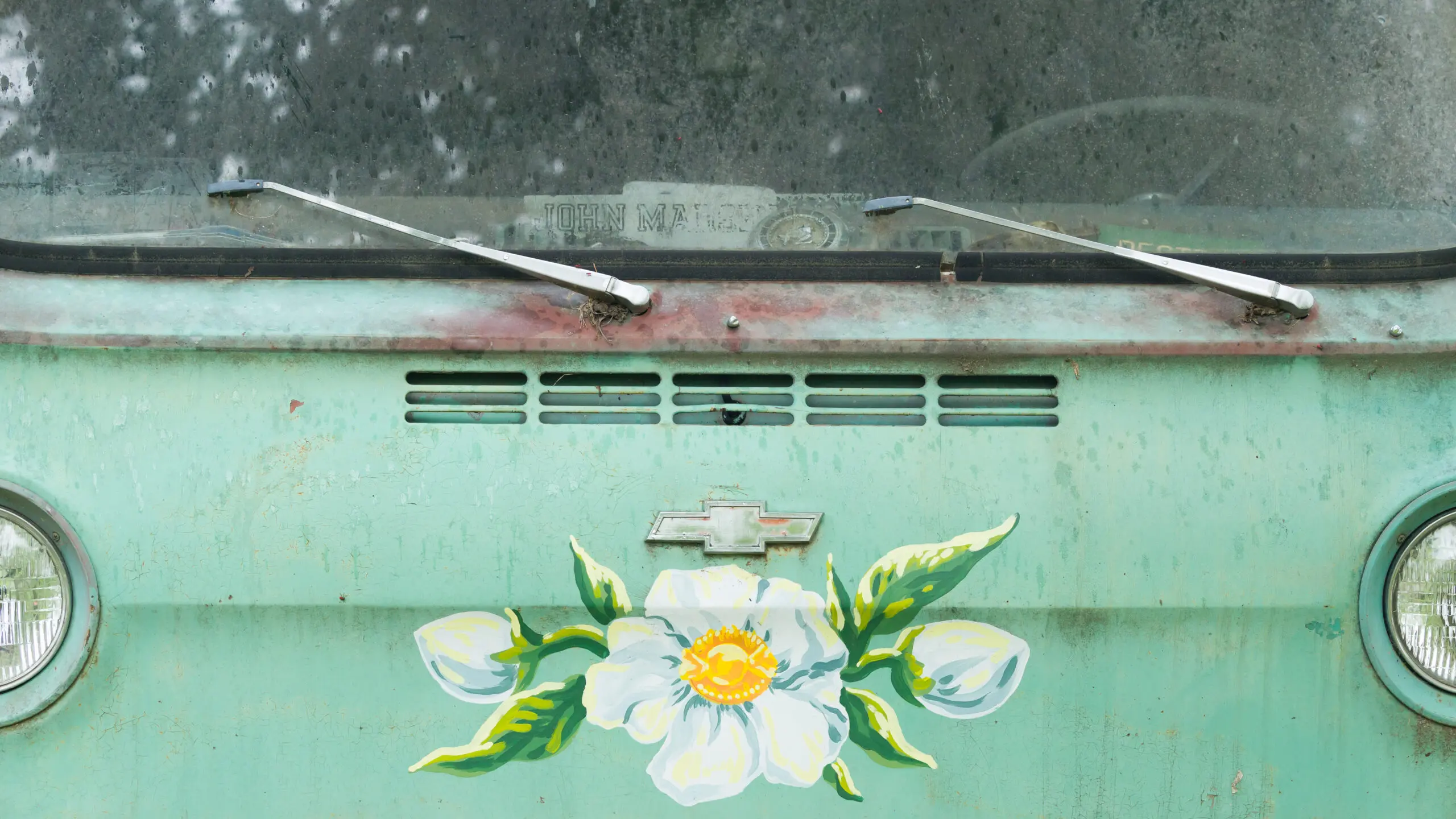 Rusty car hood with a white flower painting and windshield wipers.